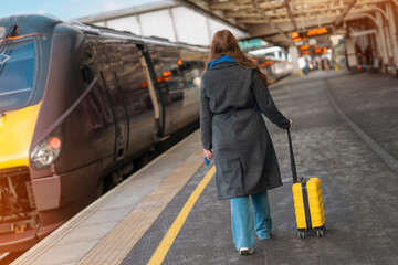 woman with yellow suitcase walking to train at railway station on platform. Travel concept