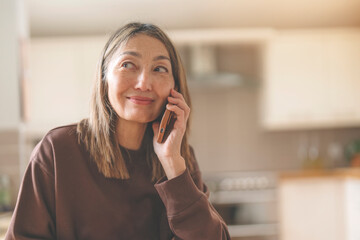 smiling asian woman talking on phone in kitchen at home
