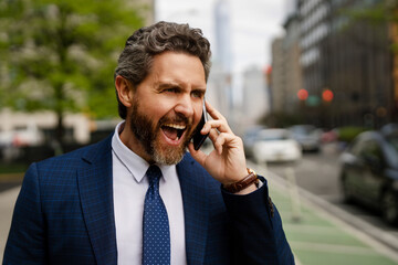 Anger Businessman with phone outdoor. Angry Business talk. Anger Man walk down street talking on...