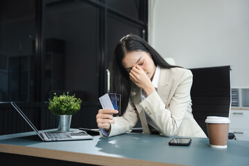 Serious woman cover her face after stressed with credit card debt sit at workplace desk in office...