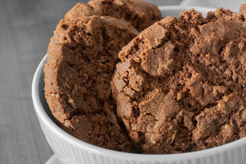 Chocolate flavoured cookies, with chocolate chips, in a green bowl on a tablecloth with a wooden background.