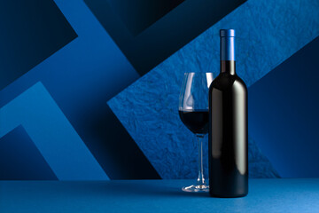Bottle and glass of red wine on a blue background.