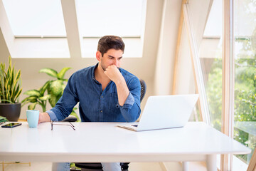 Thinking businessman sitting at desk with his laptop and working from home