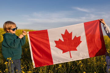 Canadian flag against the backdrop of a blooming rapeseed field. Happy Independence Day . Pride, freedom, patriotism. Travel around the country. Pride of the nation, love for the Motherland