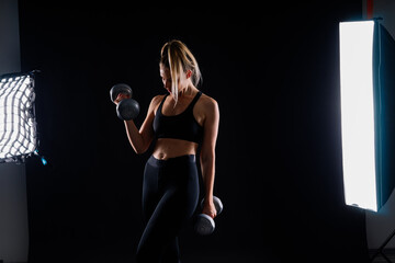 Strong woman working out with dumbbells, flexing her arm. Photo of sporty female in sportswear.