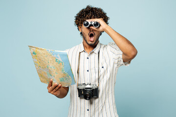 Traveler amazed Indian man in white casual clothes hold read map use binocular isolated on plain...