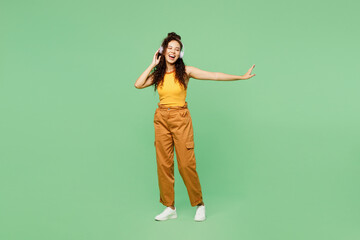 Full body young woman of African American ethnicity wear yellow tank shirt top listen to music in headphones dance isolated on plain pastel light green background studio portrait. Lifestyle concept.