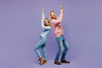 Full body young couple two friends family man woman wear pink blue casual clothes together do winner gesture celebrate clenching fists dancing isolated on pastel plain light purple background studio.