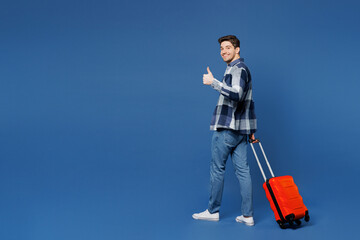 Traveler sideways man wear shirt casual clothes hold suitcase bag show thumb up isolated on plain...