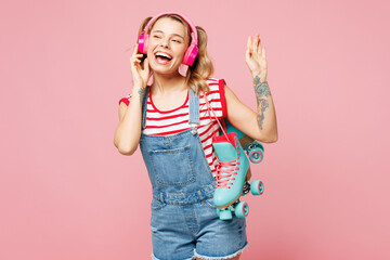 Young happy woman wear red t-shirt denim overalls casual clothes hold blue rollers listen to music...