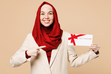 Young happy Arabian Asian Muslim woman wear red abaya hijab suit clothes hold point on gift coupon...