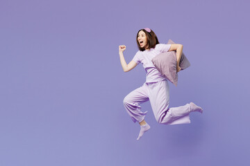 Fototapeta premium Full body side view young calm woman wear pyjamas jam sleep eye mask rest relax at home jump high run fast hold pillow isolated on plain pastel purple background studio. Good mood night nap concept.