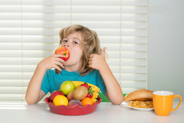 Funny child eating apple. Child in the kitchen at the table eating vegetable and fruits during the dinner lunch. Healthy food, vegetable dish.