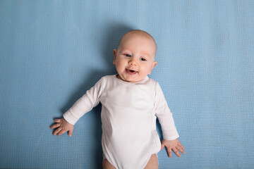 Portrait of an adorable baby lying on a mat on the floor, looking at the camera and smiling.