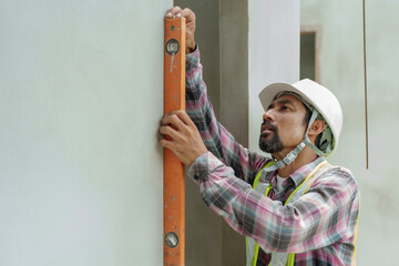 Concentrated male builder in safety gear aligns wall with level, serious expression, commitment to...