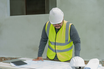 Male construction supervisor in vest reviews blueprints, attentive to detail, serious planning,...