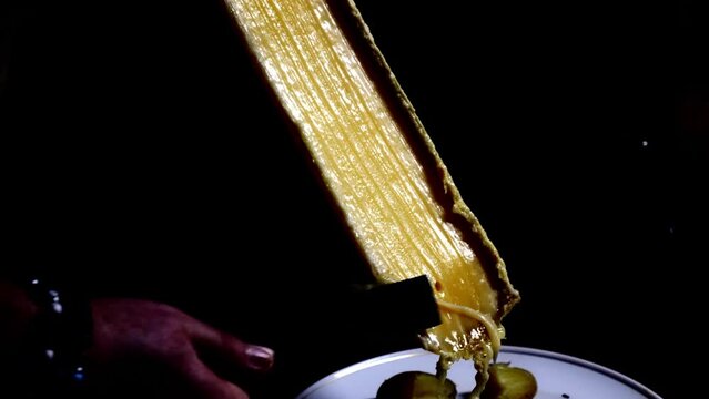 Man Scraping Swiss Traditional Melted Raclette Cheese in Canton of Valais in Switzerland.