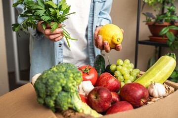 Female person unpacks grocery delivery with farm grown organic vegetables and fruits.