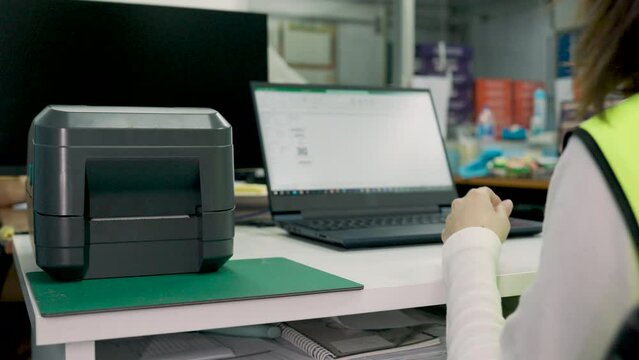 Woman uses a laptop or notebook to print bar code stickers on a bar code printer. Selective focus at sticker barcode.