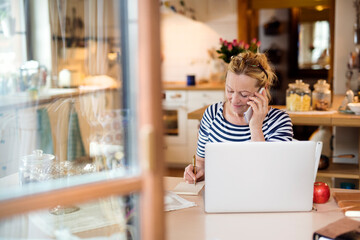 Older woman working from homeoffice, typing on laptop, making phone calls. The retiree earning extra money during retirement.