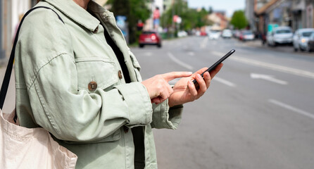 Female urban person stands near the city road and booking a taxi using her mobile app. Free floating car-sharing service online searching.