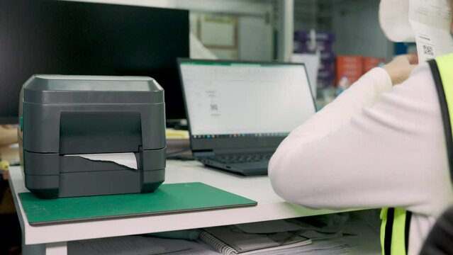 Woman uses a laptop or notebook to print bar code stickers on a bar code printer. Selective focus at sticker barcode.
