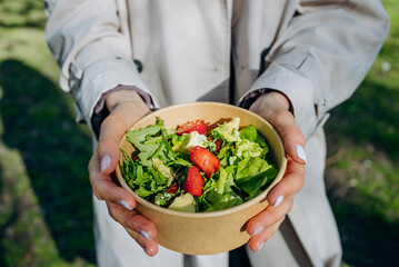 Women's hands hold a paper bowl with lettuce, strawberries and green leaves. Healthy eating...