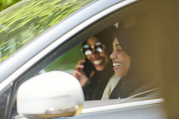 Naklejka premium Two Muslim women wearing hijab converse on a smartphone while traveling together in a car through the 
