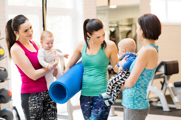 Group exercise class, mother working out with baby in gym. Moms staying active while boding with babies. New mom friends.