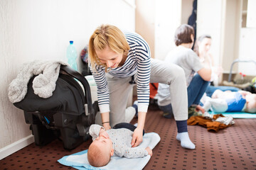 Mother changing diaper after group exercise class. Moms staying active, working out with baby in...