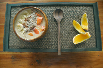 A healthy tropical vegan breakfast smoothie bowl with banana and papaya fruit toppings served on a wooden bowl and woven tray showing a healthy sustainable lifestyle