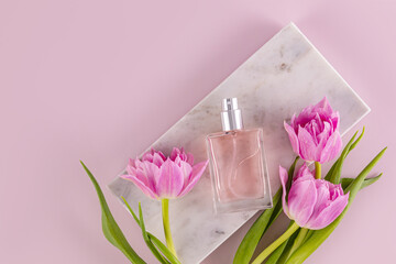 An elegant bottle of eau de parfum or women's perfume lies on a marble rectangular podium with tulips. Fragrance presentation. Top view.