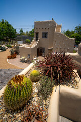 Modern stone building with a textured wall, featuring an array of desert plants under a bright sky.