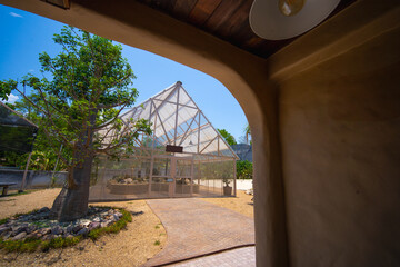 View through a curved archway showing a geodesic dome, greenhouse in a tranquil outdoor setting,...