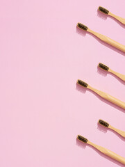 Repetitive pattern of bamboo toothbrushes on pink background with copy space.