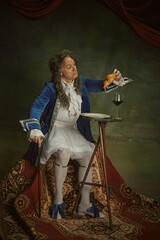 Senior man, dressed baroque style clothe with curious expression eating croissant and drinks wine...