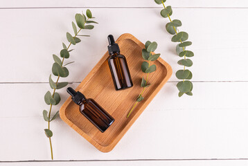 Two cosmetic bottles with a dropper on a wooden tray with a natural product based on eucalyptus oils for facial skin care. Top view.