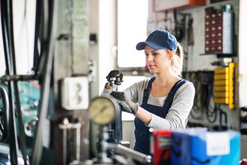 Female auto mechanic repairing, maintaining car. Beautiful woman working in a garage, wearing blue...