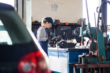 Female auto mechanic repairing, maintaining car. Beautiful woman working in a garage, wearing blue...