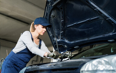 Female auto mechanic repairing, maintaining car. Beautiful woman working in a garage, wearing blue...