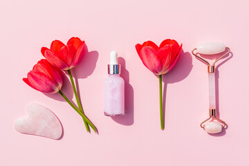 Cosmetic set for home massage and skin care of the face and neck. quartz massager, gua sha, natural oil on a pink background with flowers. Flat lay