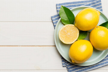 Fresh cutted lemon and whole lemons over round plate on colored background. Food and drink...