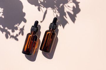 Two cosmetic bottles with a moisturizing serum to moisturize the skin of the face on a beige background and sunlight. A copy space. Empty bottle lay