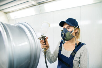 Female car painter, paingting vehicles in auto body shop. Young woman holding spray gun, spraying...