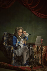Elderly man, dressed as king in classical attire and glasses sitting watching film in modern laptop...