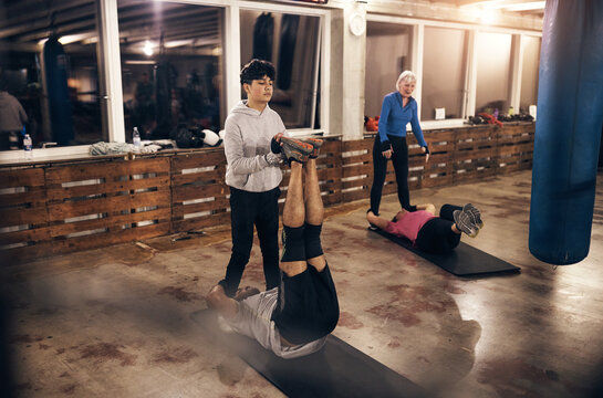 A group of diverse people doing an ab workout with partners in a boxing gym
