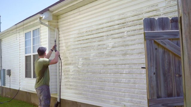 Man cleaning house with power washer. Wide shot.