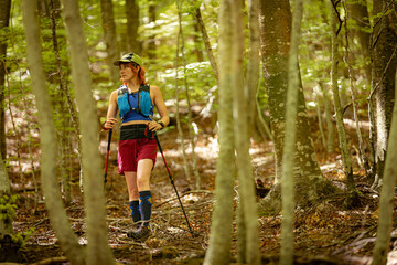 Obraz premium A woman is walking through a forest with a backpack on her back. She is wearing a blue shirt and red shorts