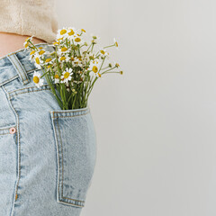 Young pretty woman with chamomile flowers bouquet in jeans pocket