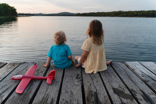 Brother and sister sitting on pier over lake